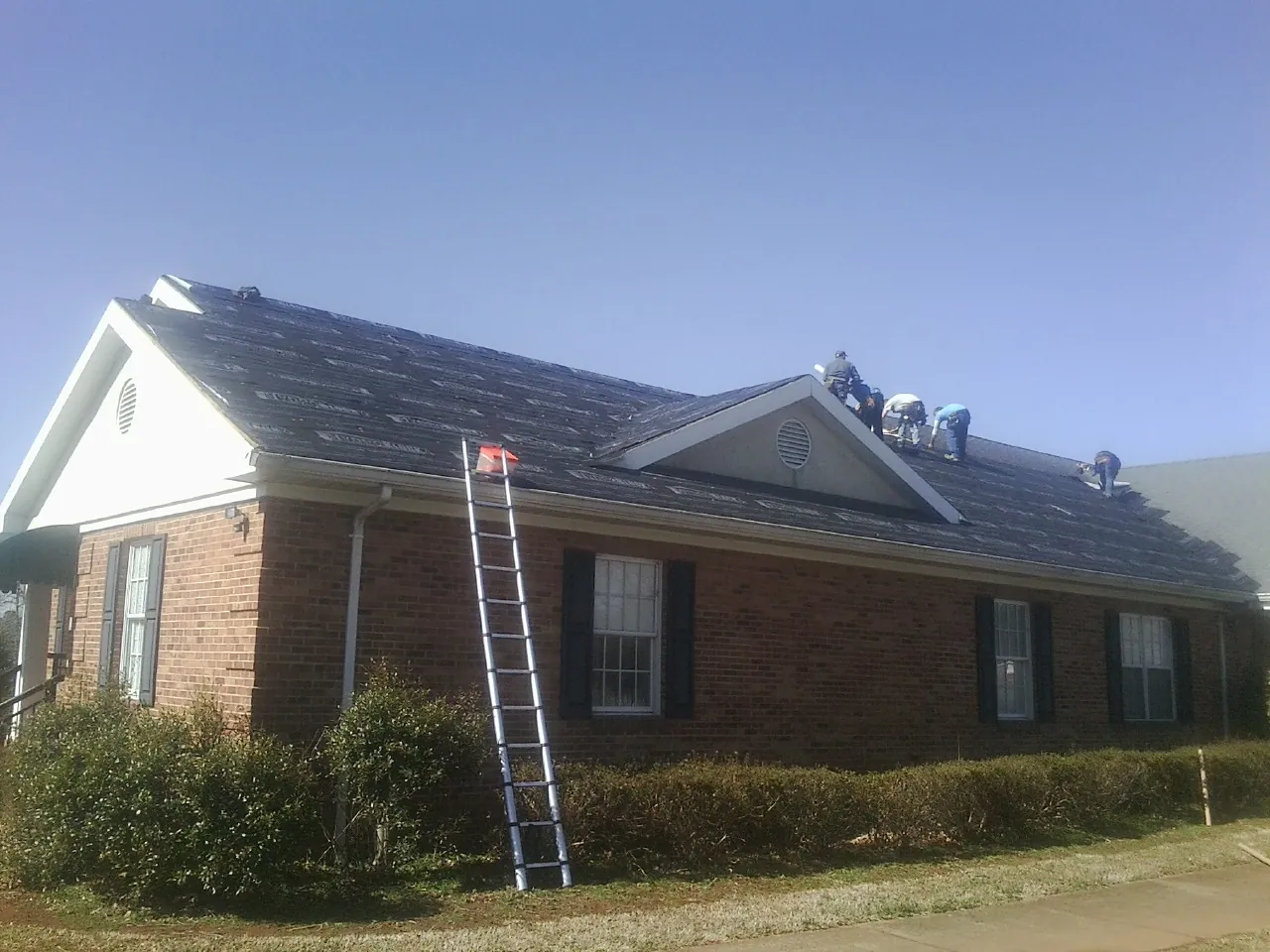 Crew tearing shingles off a brick ranch roof with a ladder set — Metal Roof Repair work by our crew in Preston