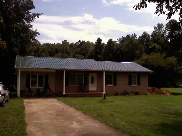 Dark green metal roof on a brick ranch with a covered porch in Preston